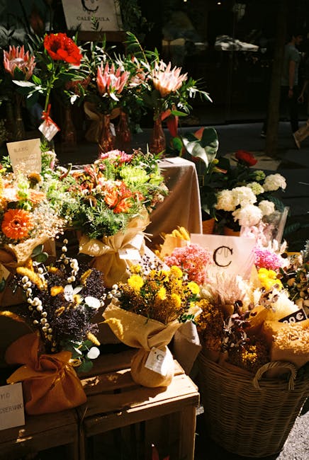 A display of vibrant floral arrangements featuring a variety of fresh flowers, including bright red gerbera daisies, pink and white lilies, yellow chrysanthemums, white baby's breath, and purple stati